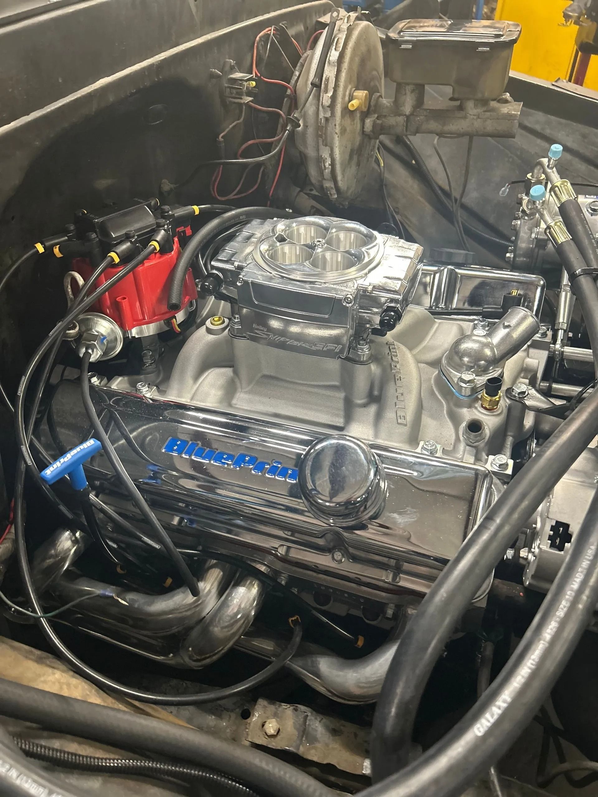 A clean, chrome-accented V8 engine sits inside a vehicle engine bay, featuring a bright red distributor and blue trim.
