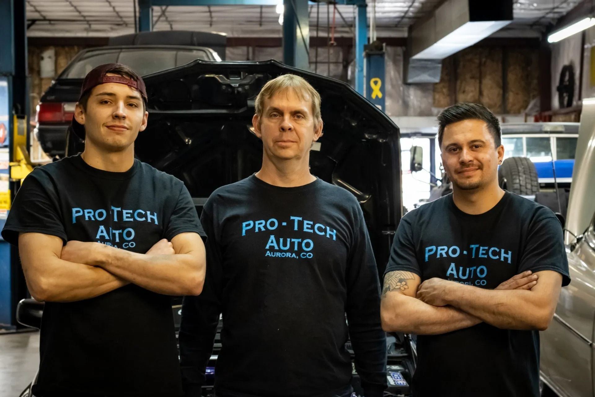 Three people in branded shirts standing inside an automotive repair shop with vehicles in the background.