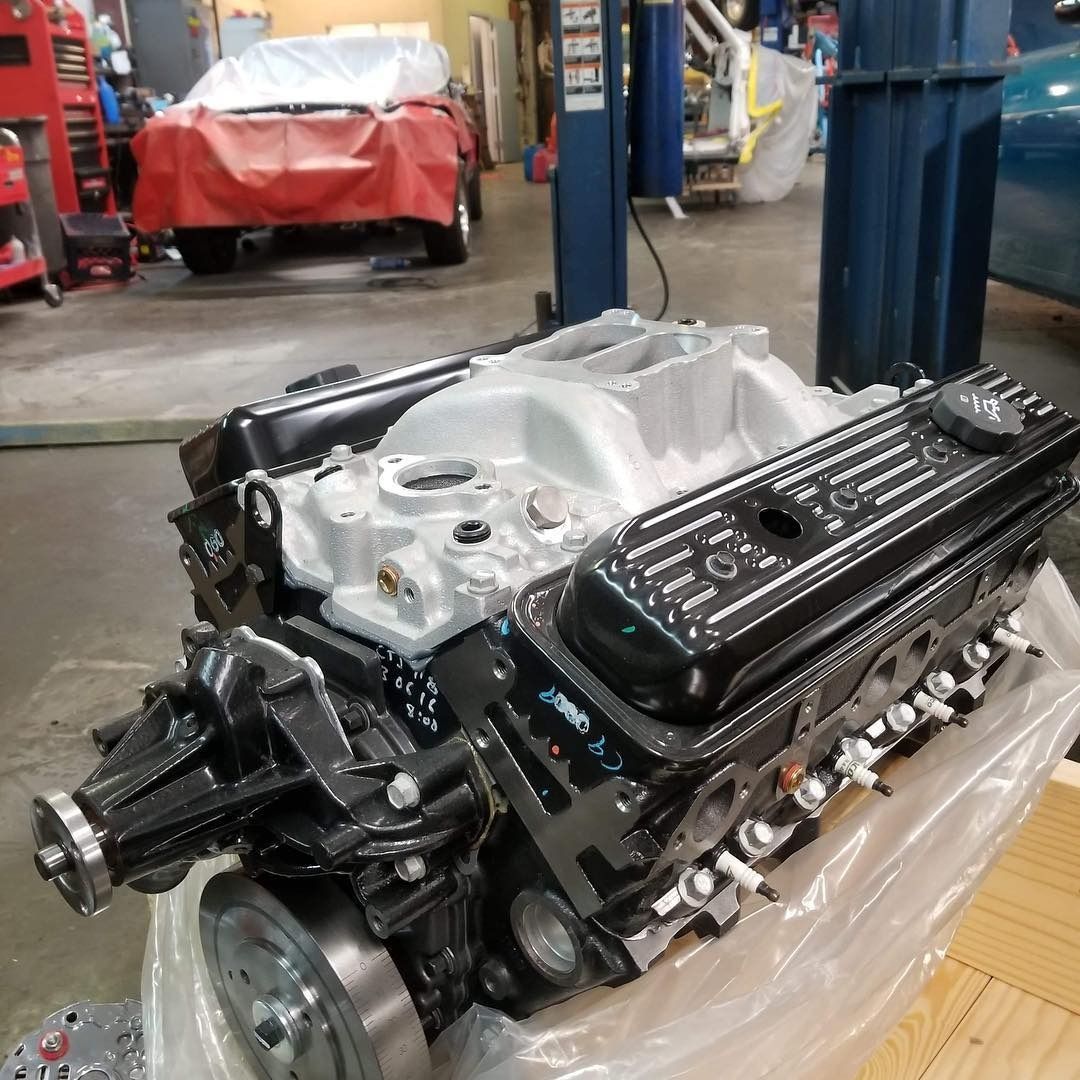 A refurbished black and silver V8 car engine sits on plastic wrap in an automotive repair shop.
