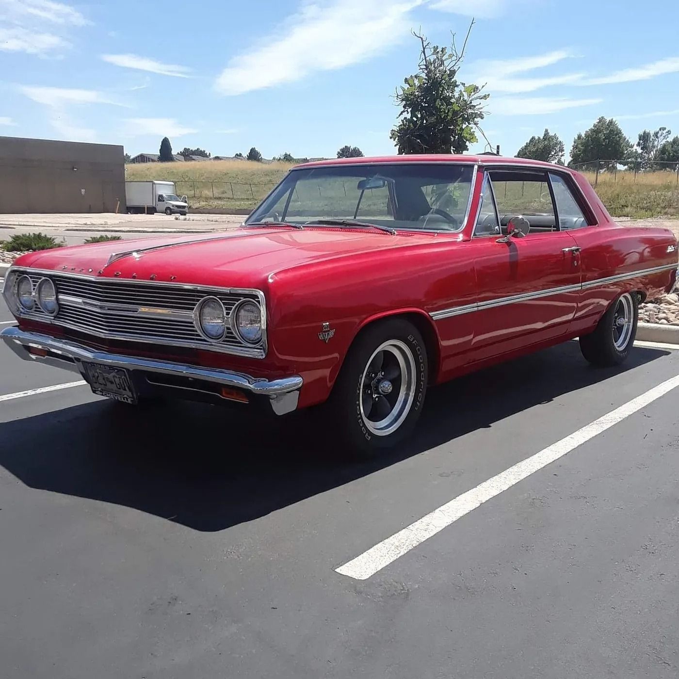 A bright red classic Chevrolet Chevelle parked in an outdoor parking lot on a sunny day.