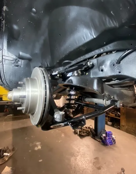 A close-up of a black vehicle chassis showing a newly installed disc brake assembly, control arm, and coil-over shock.