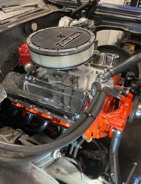 A high-angle view of a clean V8 engine with a prominent black Edelbrock air cleaner, chrome valve covers, and orange block.