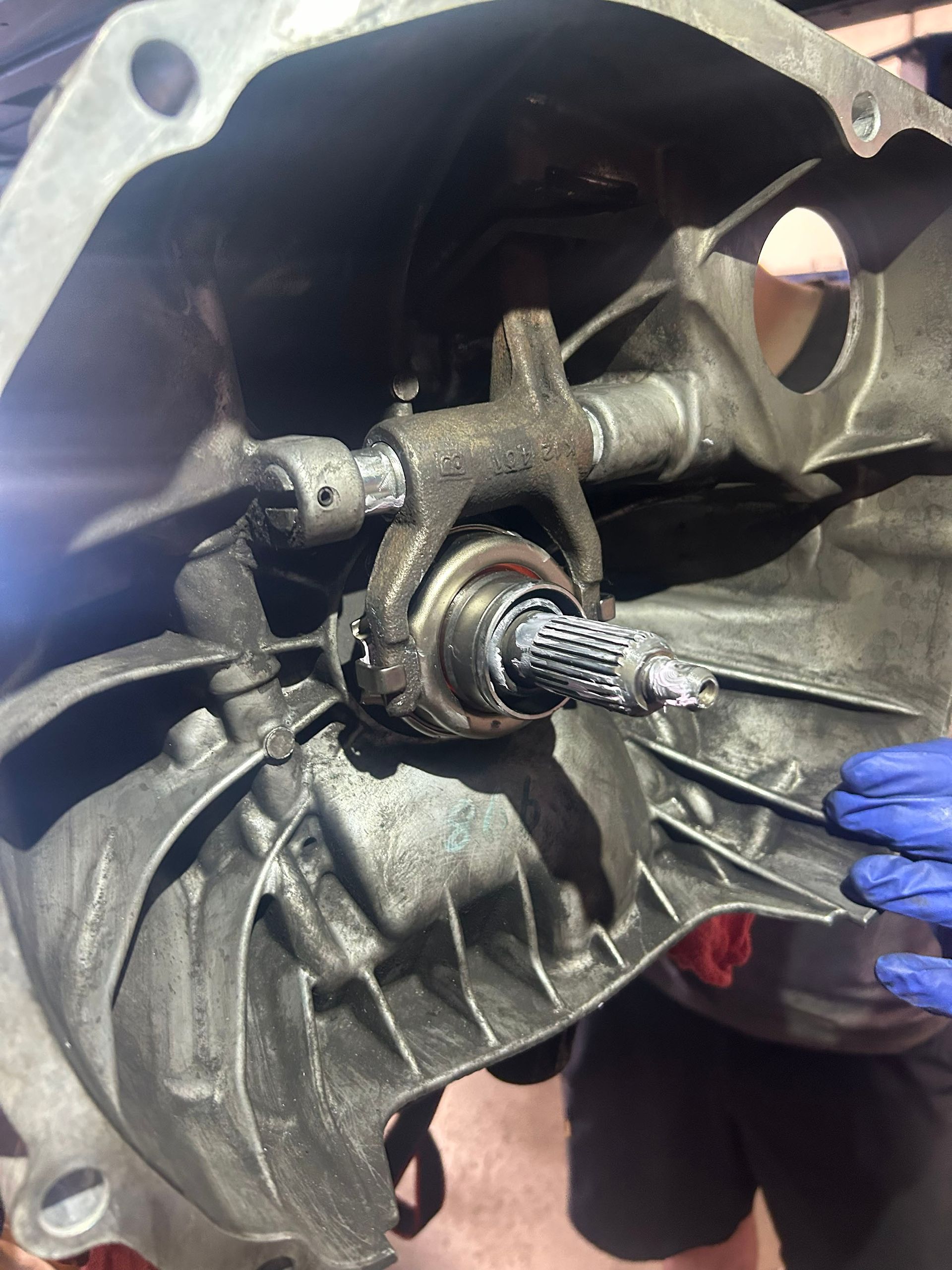 An inside view of a transmission bell housing showing a clutch release bearing on the input shaft, held by a fork.