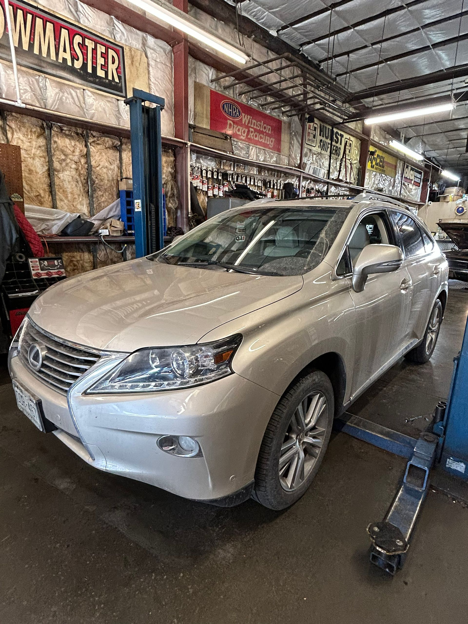 A silver Lexus RX SUV parked inside an auto repair shop with lift equipment visible.