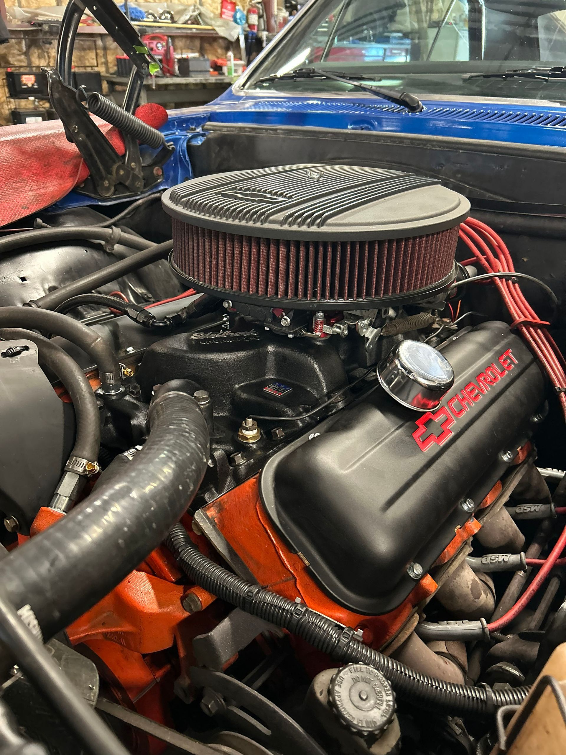 A close-up of a classic Chevrolet V8 engine with a black air cleaner, orange block, and black valve covers.