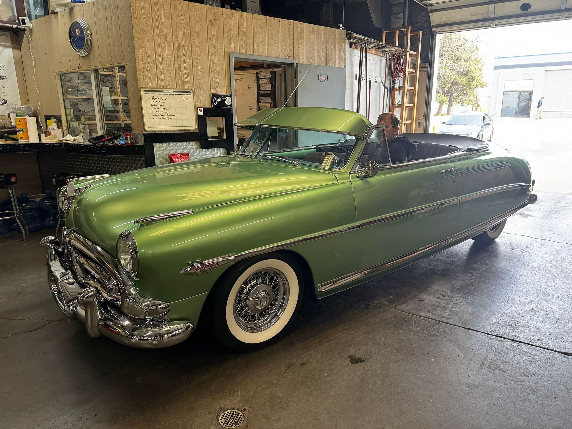 A metallic lime-green classic convertible parked inside an auto shop with a person sitting in the driver’s seat.