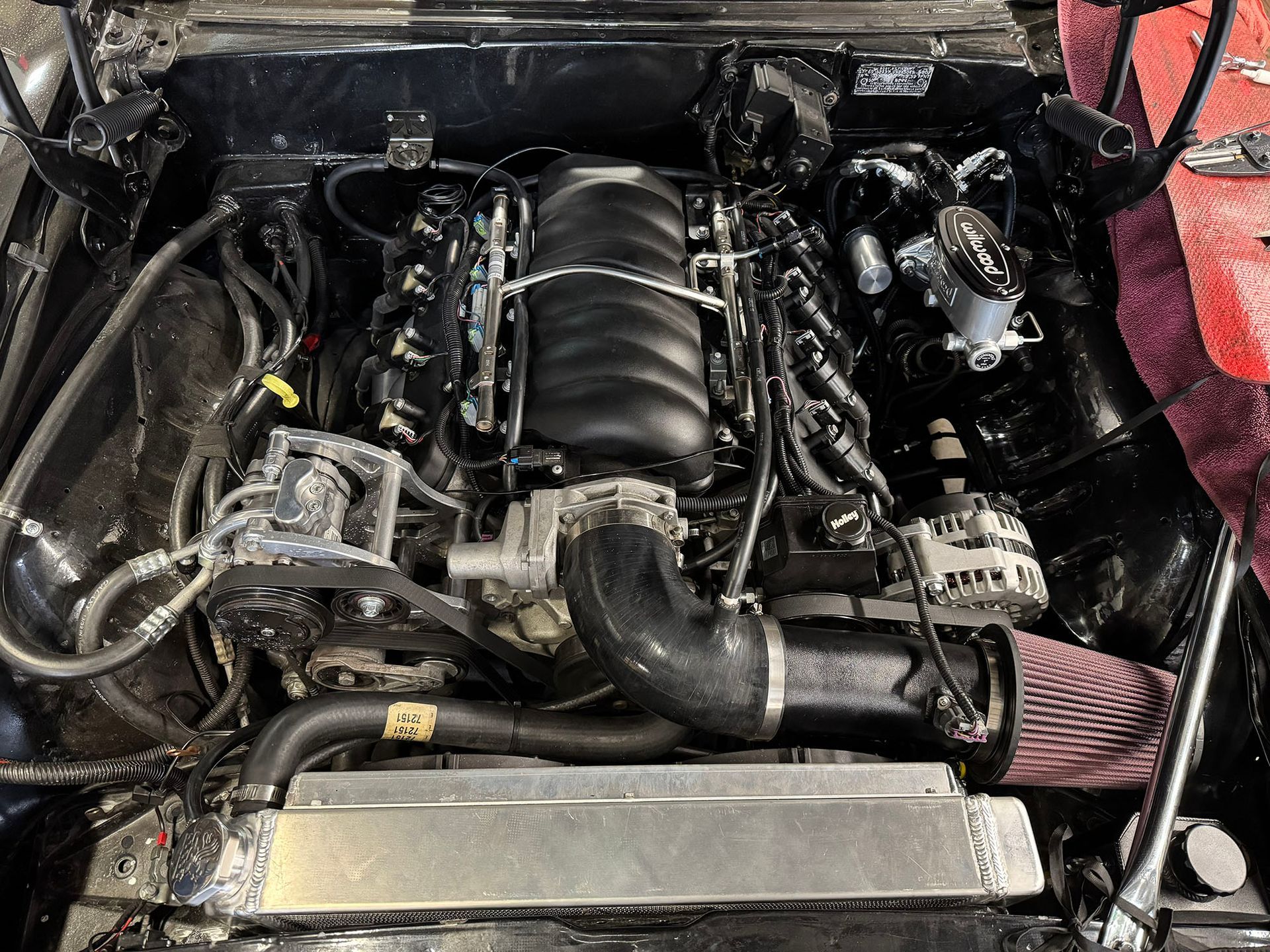 A black, modern V8 engine swapped into the clean, dark-painted engine bay of a classic muscle car.