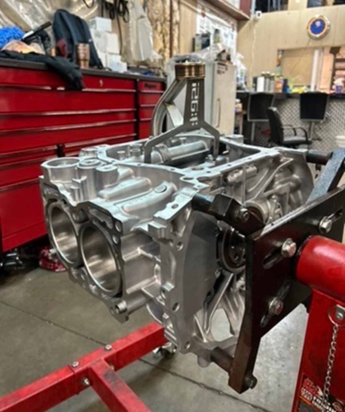 An aluminum engine block mounted on a red steel engine stand inside a workshop.