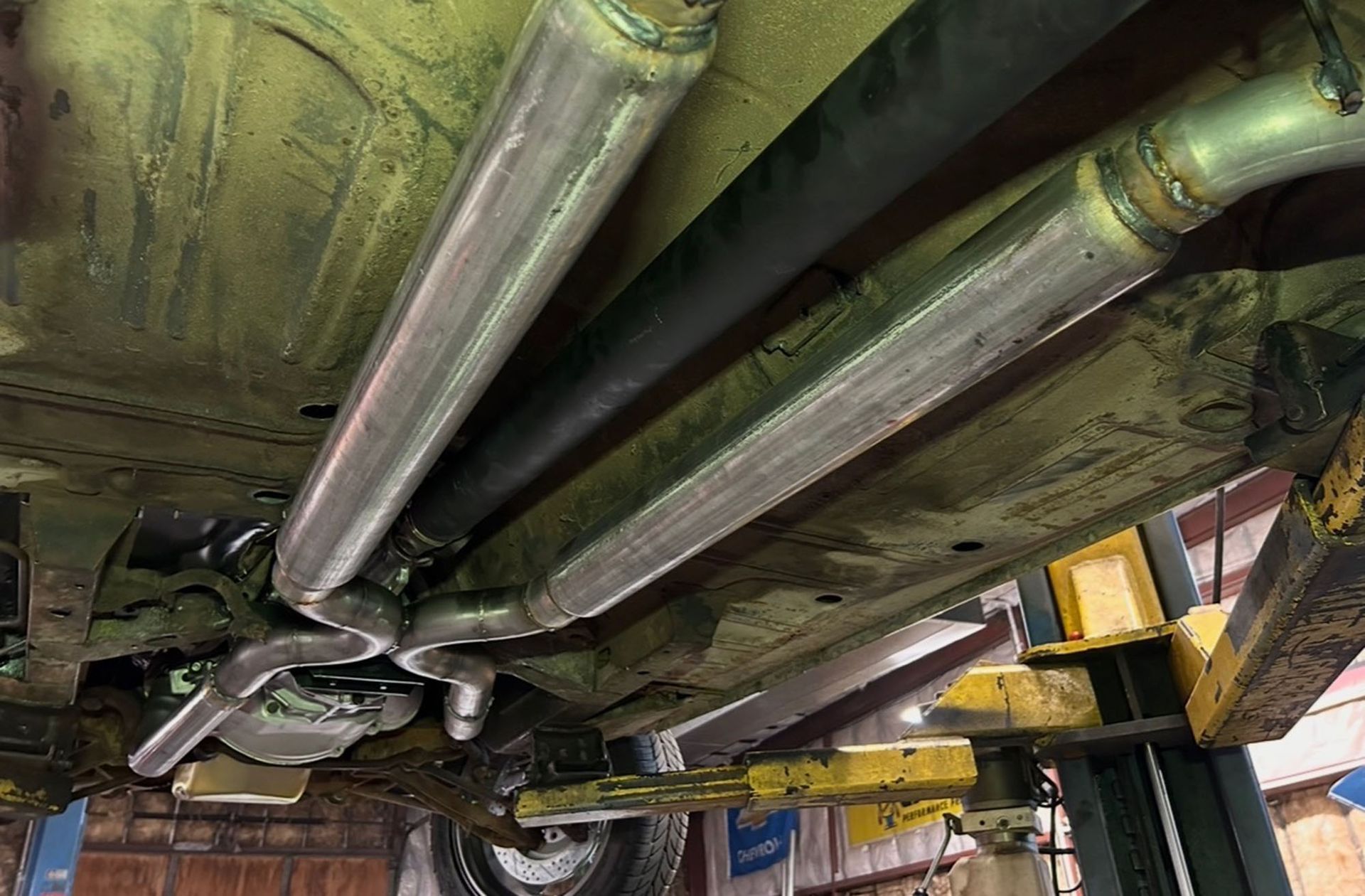 The underside of a vehicle featuring a dual exhaust system with silver metallic mufflers and an X-pipe crossover.