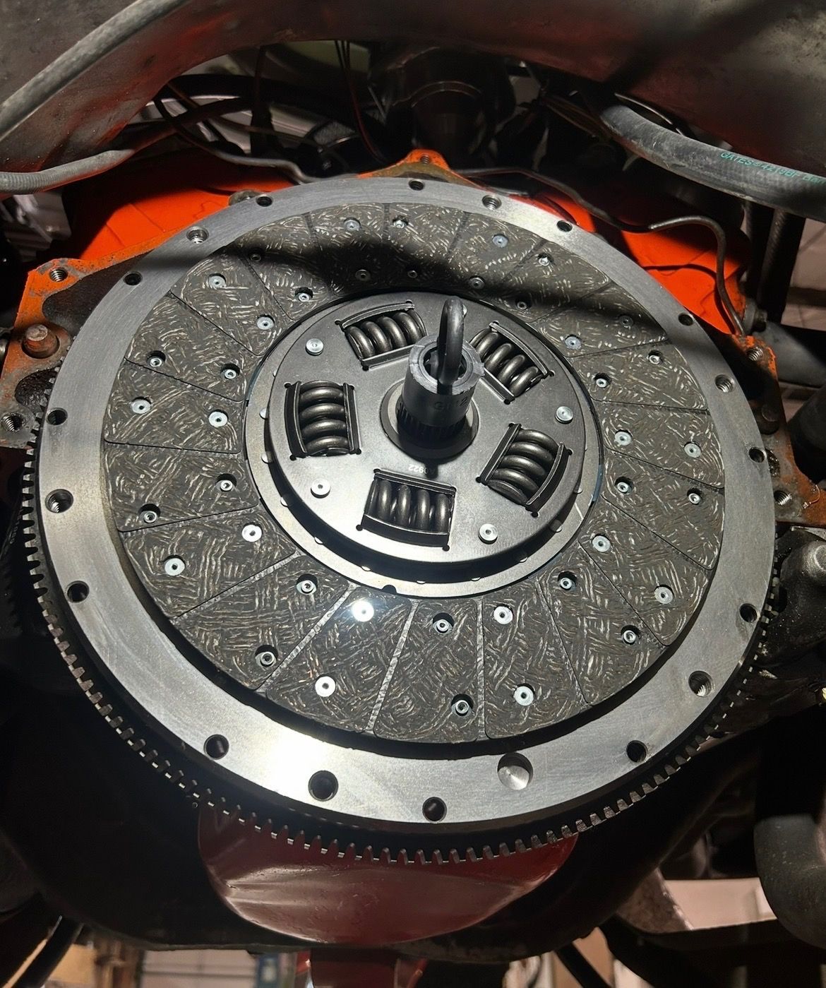 A circular clutch disc with visible springs installed onto an orange engine flywheel inside a vehicle chassis.