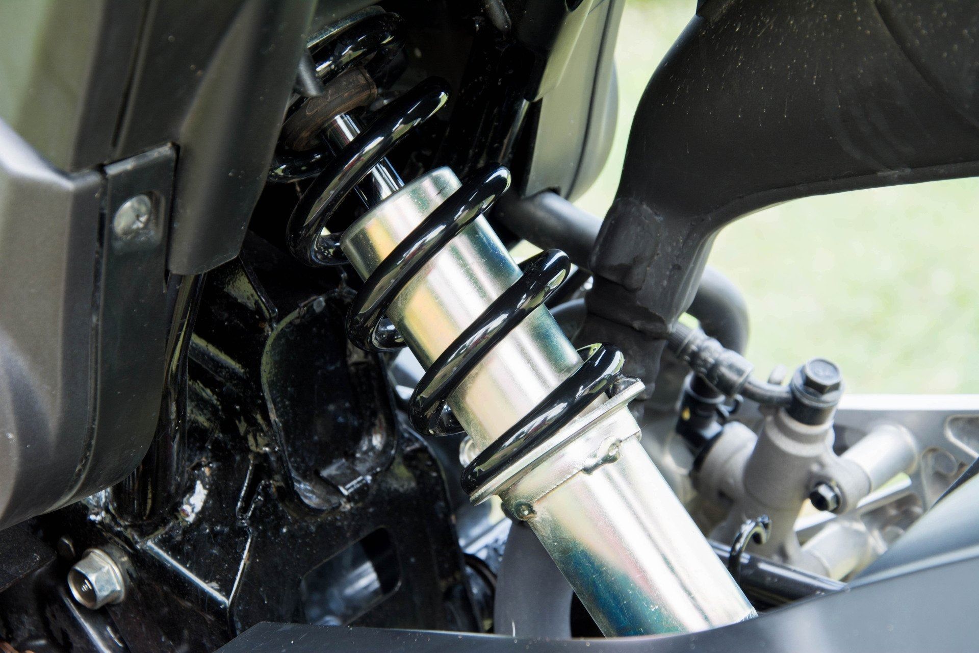 A close-up view of a motorcycle's rear mono-shock suspension system featuring a silver cylinder and a black metal coil.