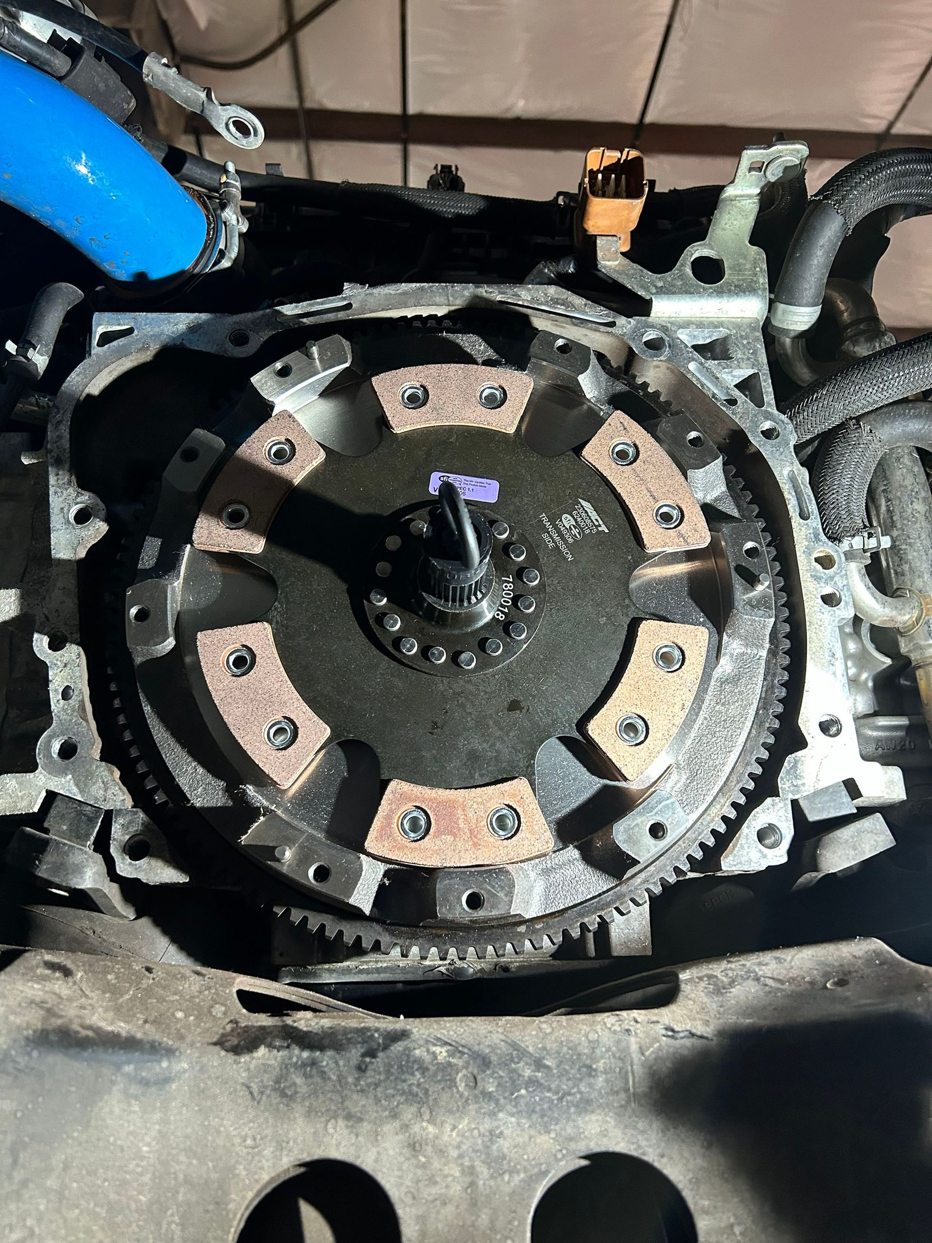 A metal engine flywheel and clutch disc with ceramic friction pads installed on a vehicle engine block.