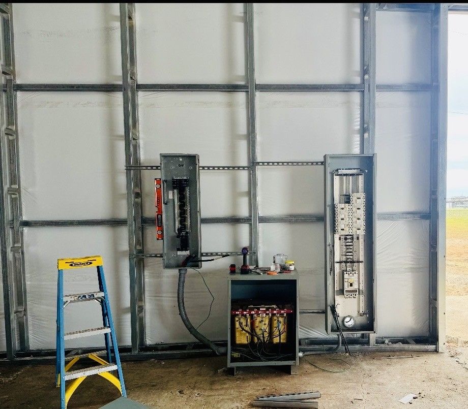 Two electrical panels and a battery backup unit mounted on the metal framing of a wall, with a stepladder to the left.