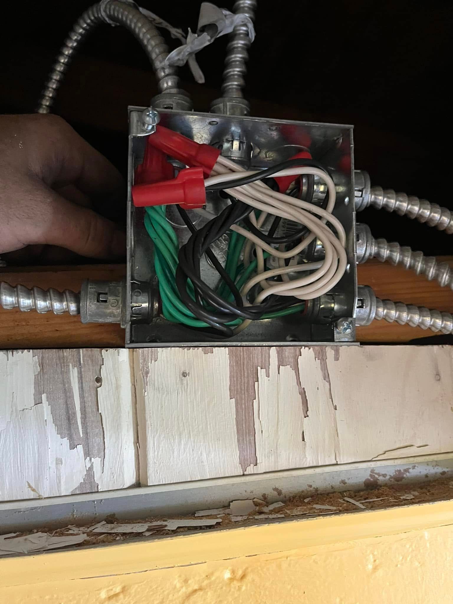 A hand reaches into a metal electrical junction box filled with black, white, and green wires connected by red wire nuts.