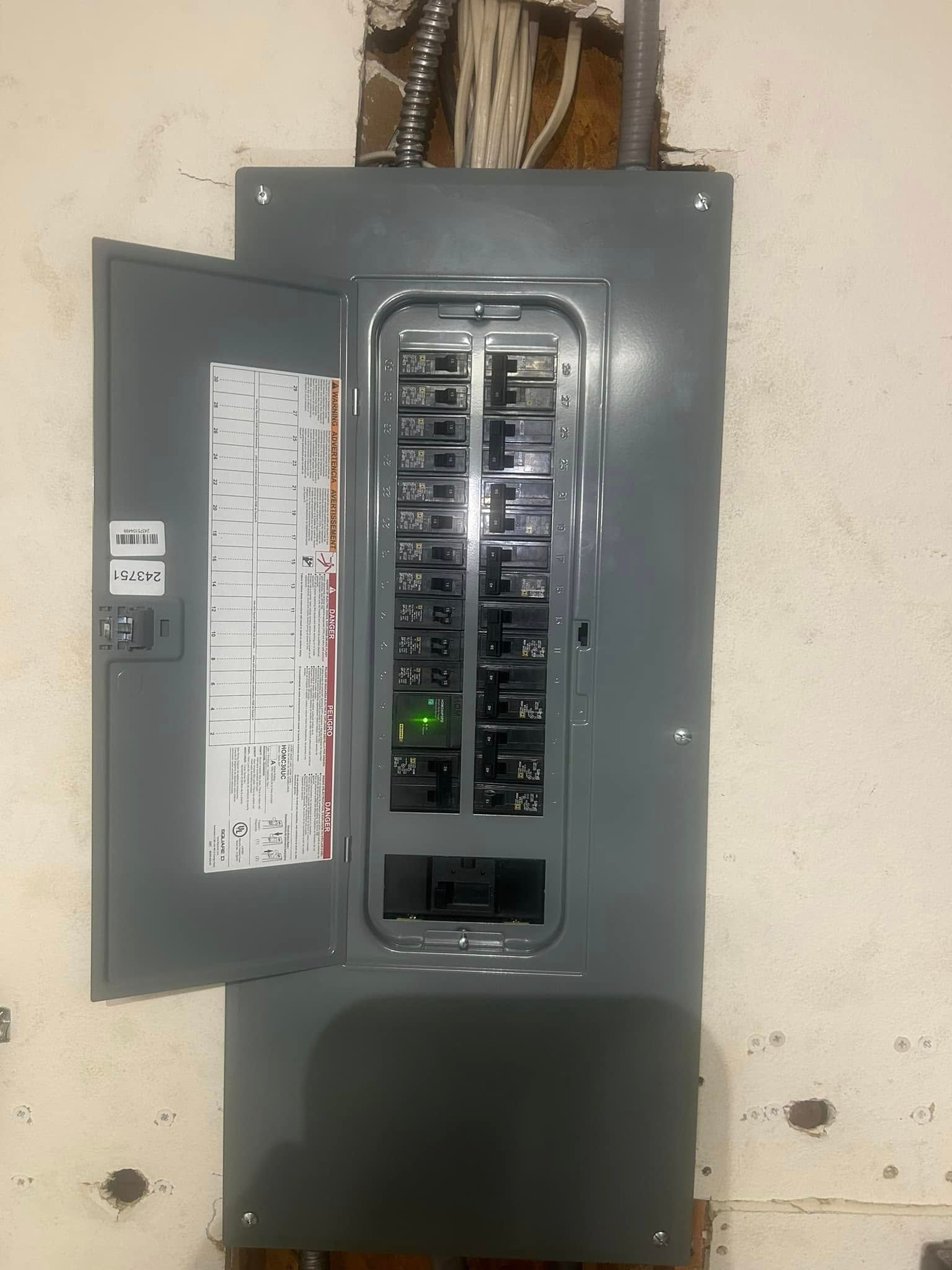 A gray electrical breaker panel mounted on a light-colored wall with its door open, showing several circuit breakers.