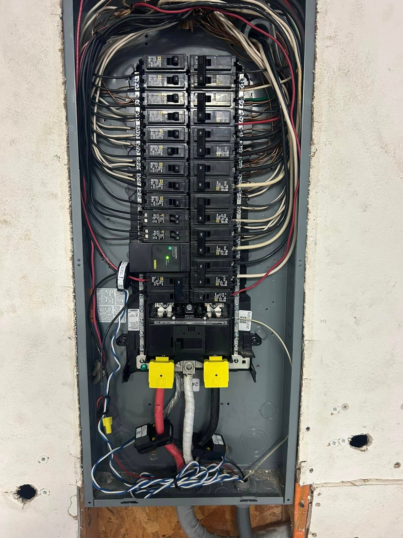An open electrical service panel showing a main breaker, multiple branch circuit breakers, and thick service wiring.