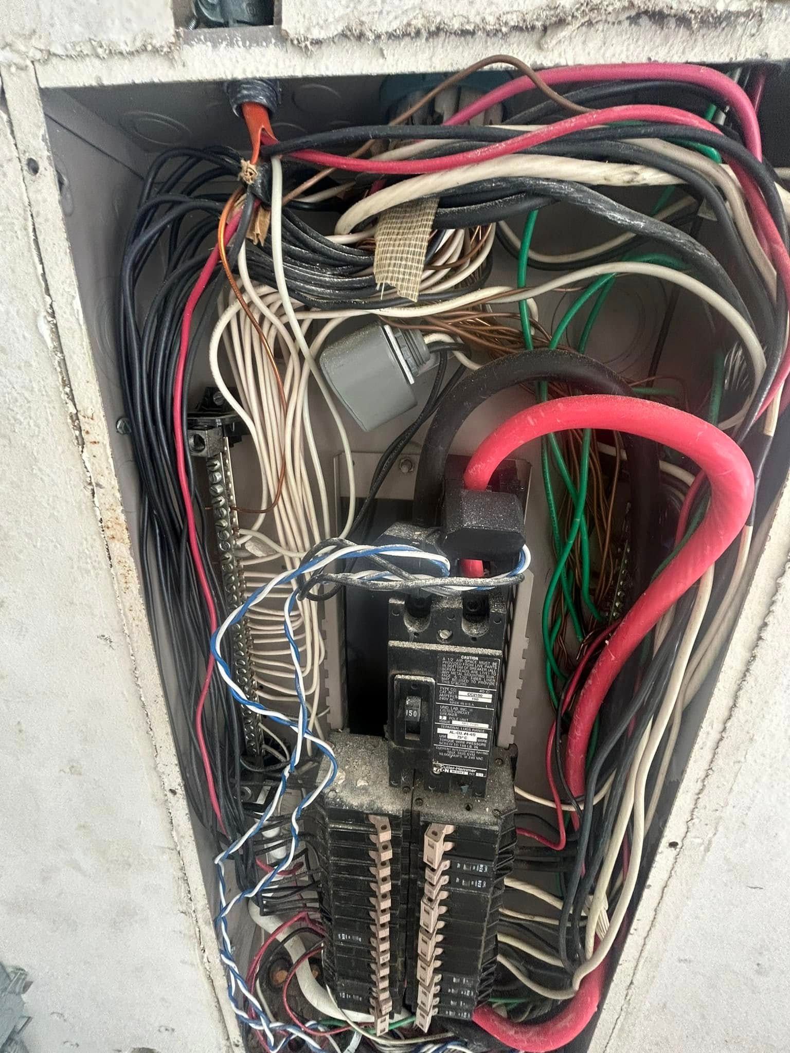 An open electrical service panel showing a dense, disorganized collection of multi-colored wiring and circuit breakers.