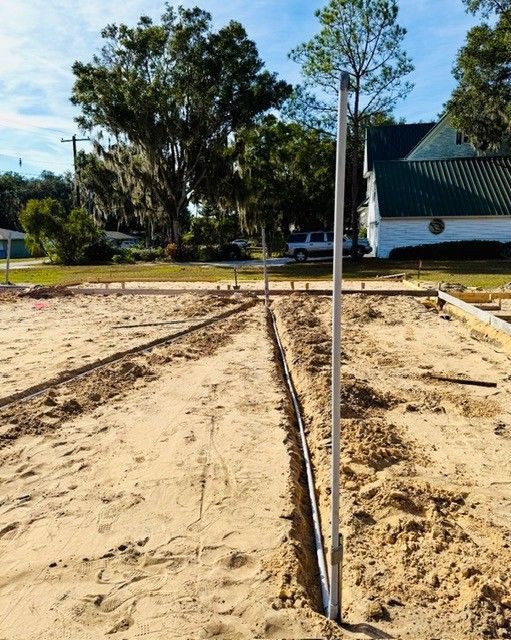 A construction site with sandy ground, wooden frame foundations, and a vertical measuring pole in a sunny, outdoor area.