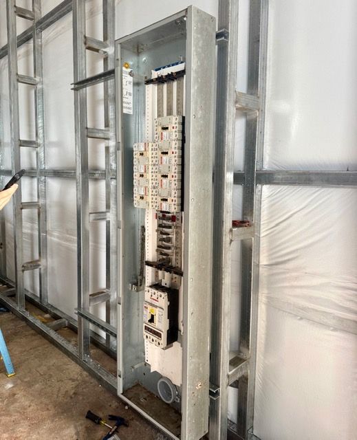 An open electrical panel box installed within a metal stud wall frame on a construction site.