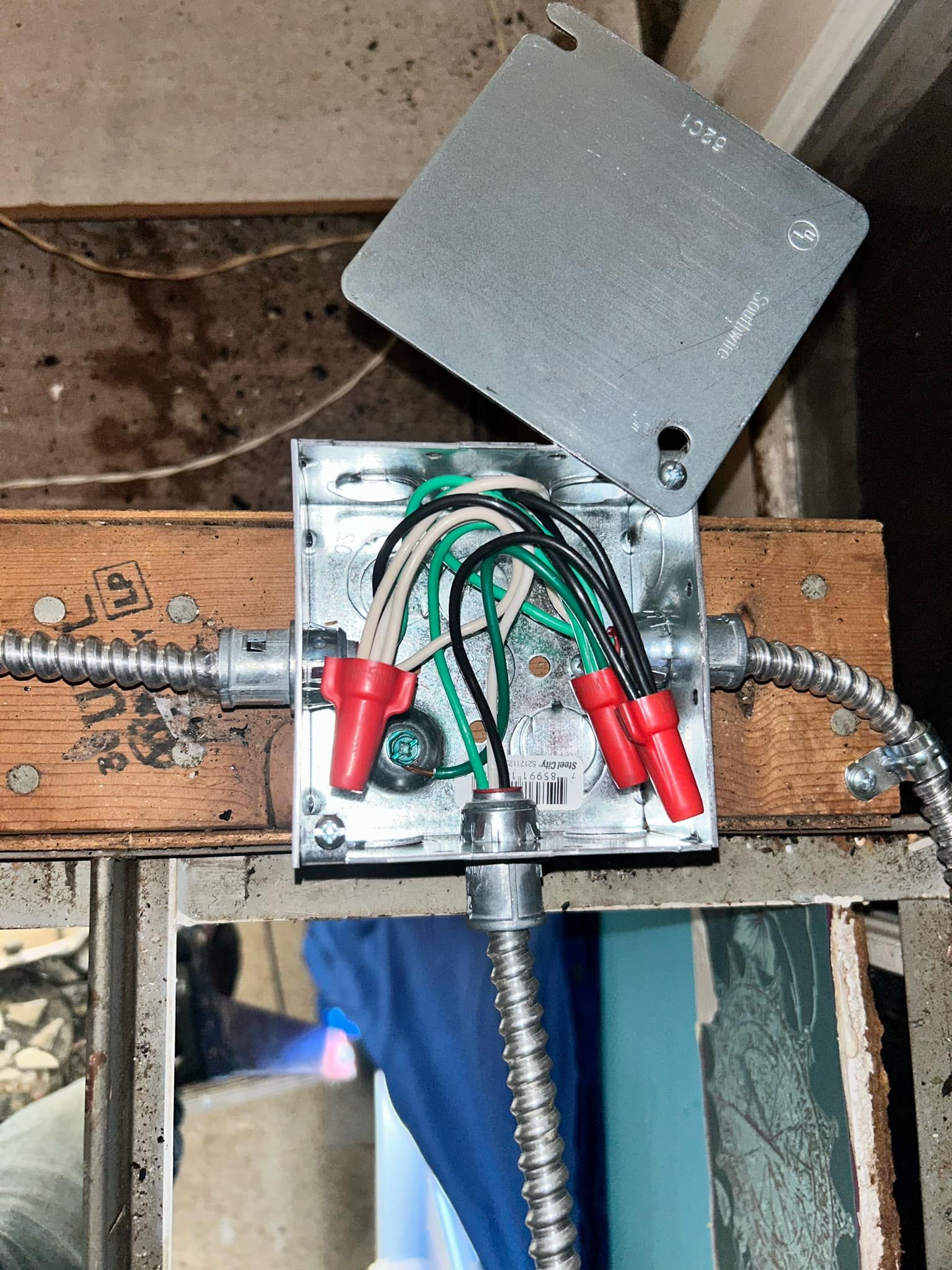 An open electrical junction box attached to a wooden beam with wires joined by red plastic wire connectors.