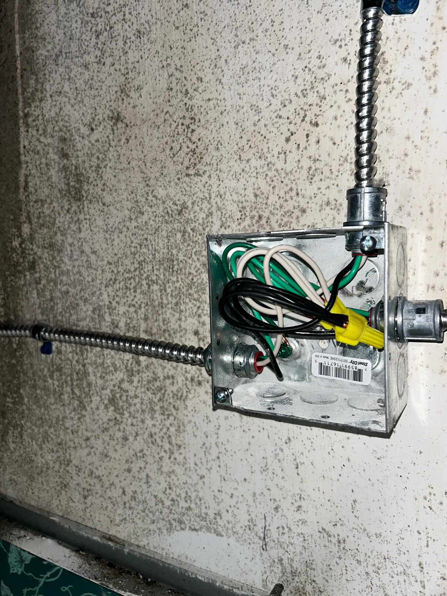 An exposed metal electrical junction box on a textured wall with wires connected by yellow wire nuts.