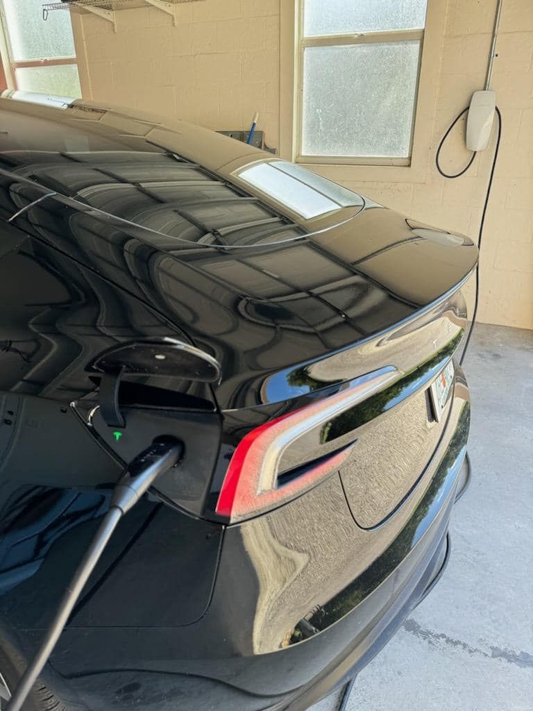 A black Tesla charging in a garage with a charging cable plugged into the rear driver-side port.