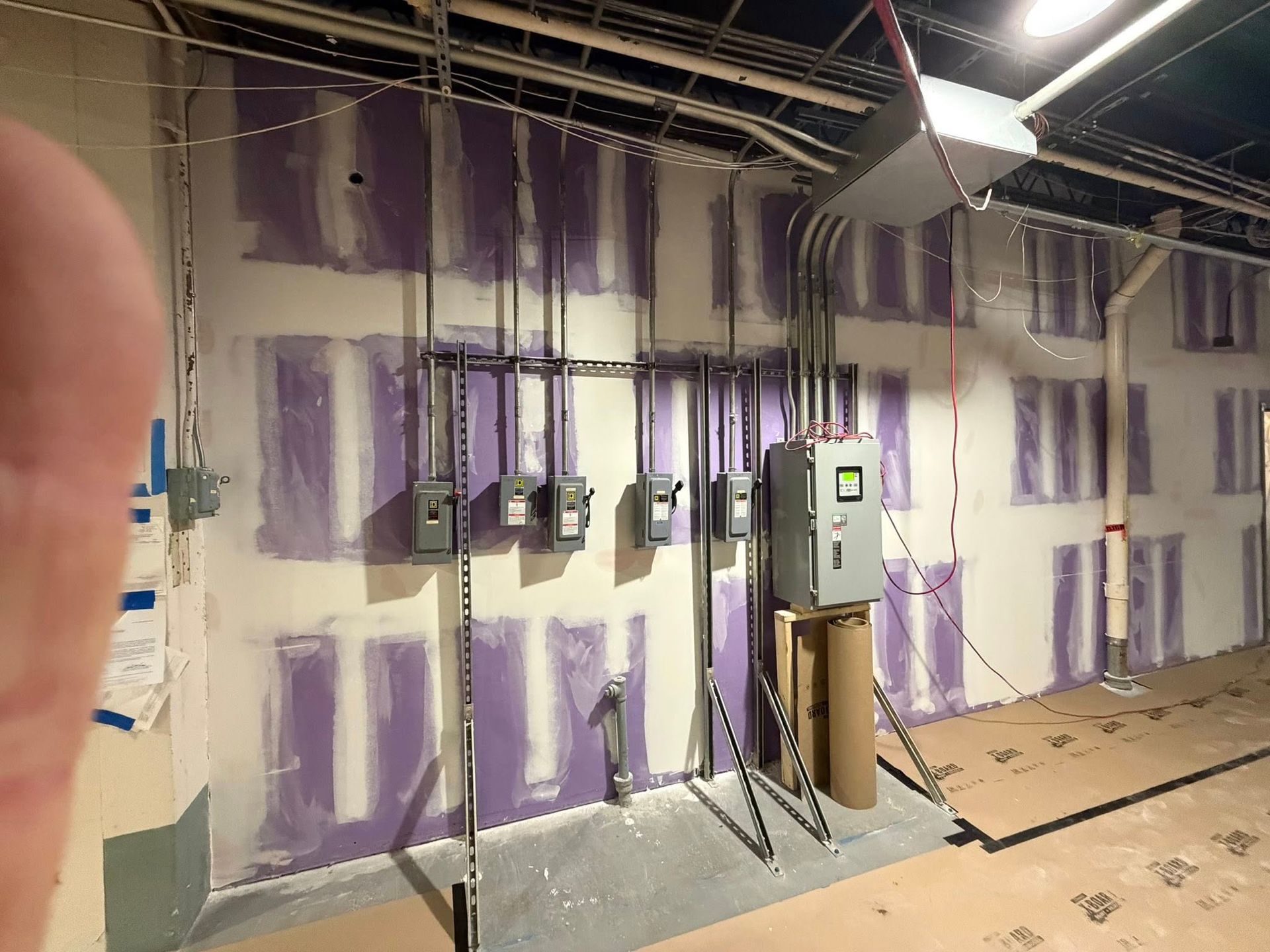 Interior wall under construction with purple-taped drywall, electrical conduits, and industrial control boxes.
