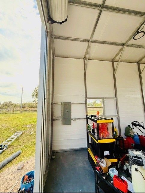 Interior of a metal storage shed showing a wall-mounted electrical panel, structural framing, and a storage rack.