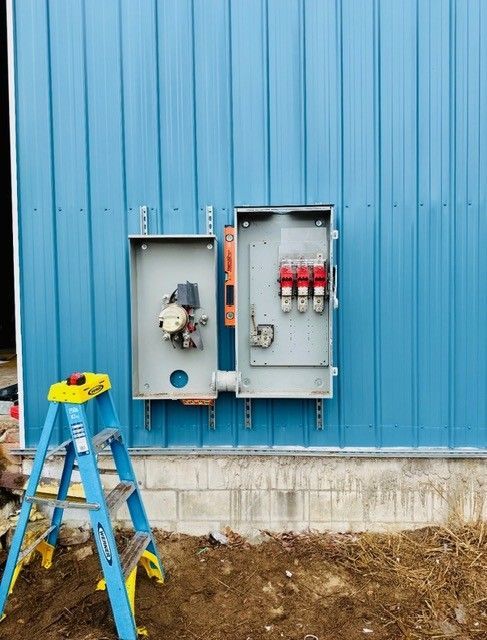 Two electrical enclosures mounted on a blue metal building wall with a blue ladder in the foreground.