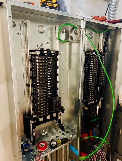 A dual-panel electrical service box with installed circuit breakers and a prominent green grounding wire.
