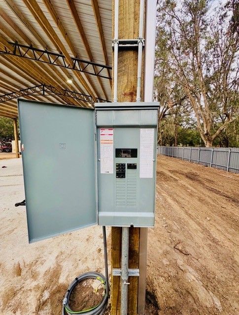 An open electrical panel mounted to a wooden utility pole outdoors under a metal roof structure.