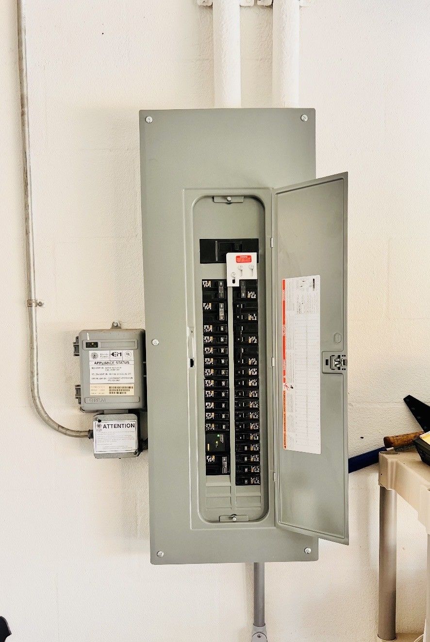 A gray electrical breaker panel mounted on a wall, with its door open to reveal a row of circuit switches.