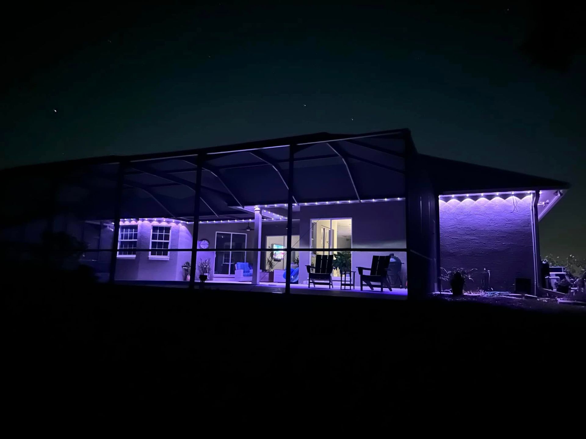 A house patio enclosed by a screen, illuminated at night by glowing purple string lights.
