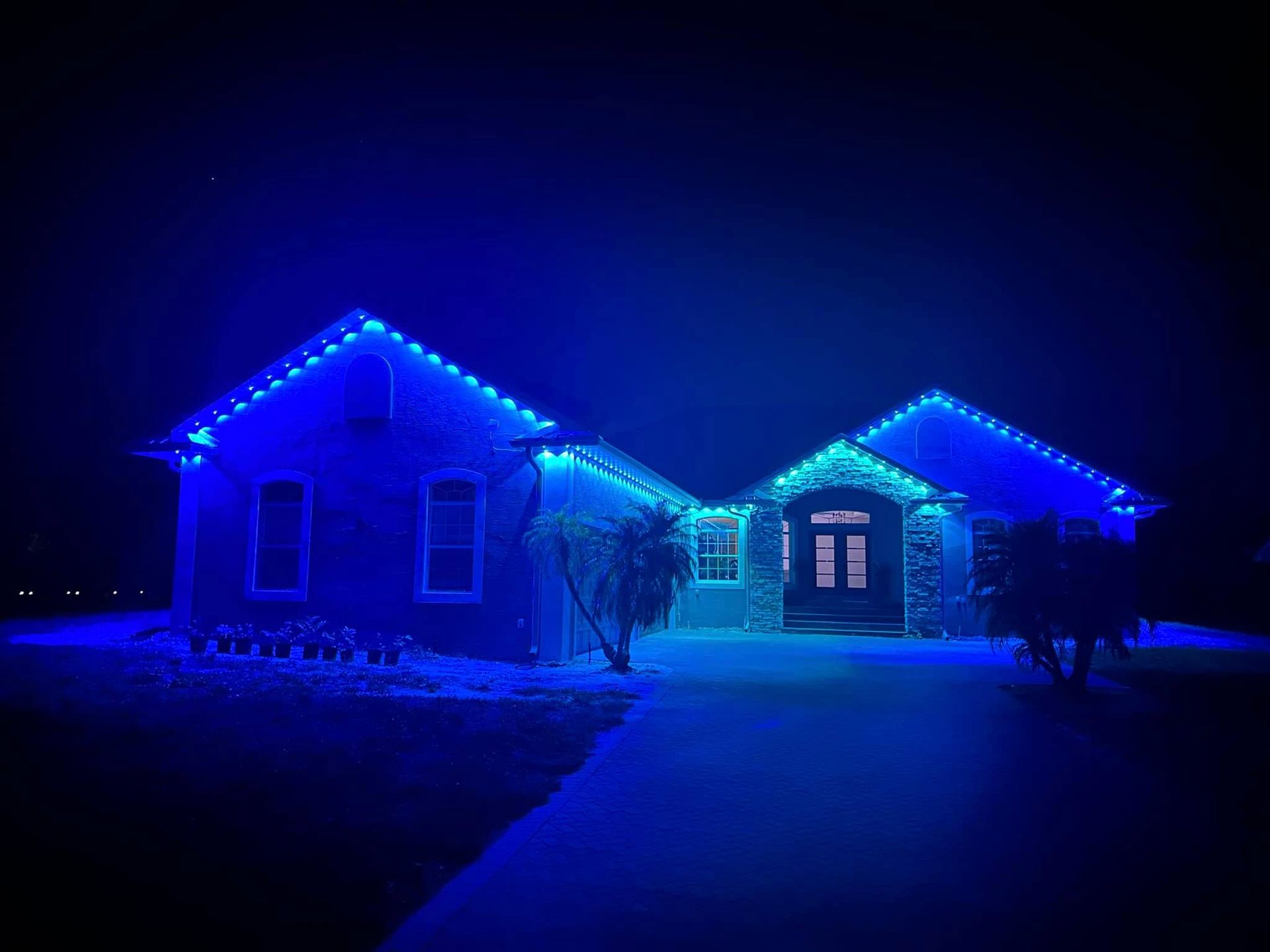 A house at night outlined with vibrant blue LED lights, illuminating the roofline, windows, and entryway.