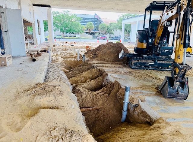 A yellow excavator parked next to a large dirt trench under a building overhang at a construction site.