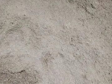 A close-up, top-down view of light gray, coarse, sandy soil or gravel with a textured, uneven surface.