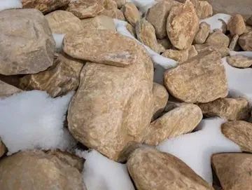 Pile of light brown rocks partially covered in snow.