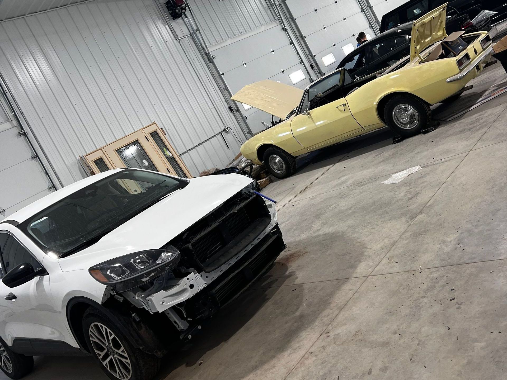 A white car is parked next to a yellow car in a garage.