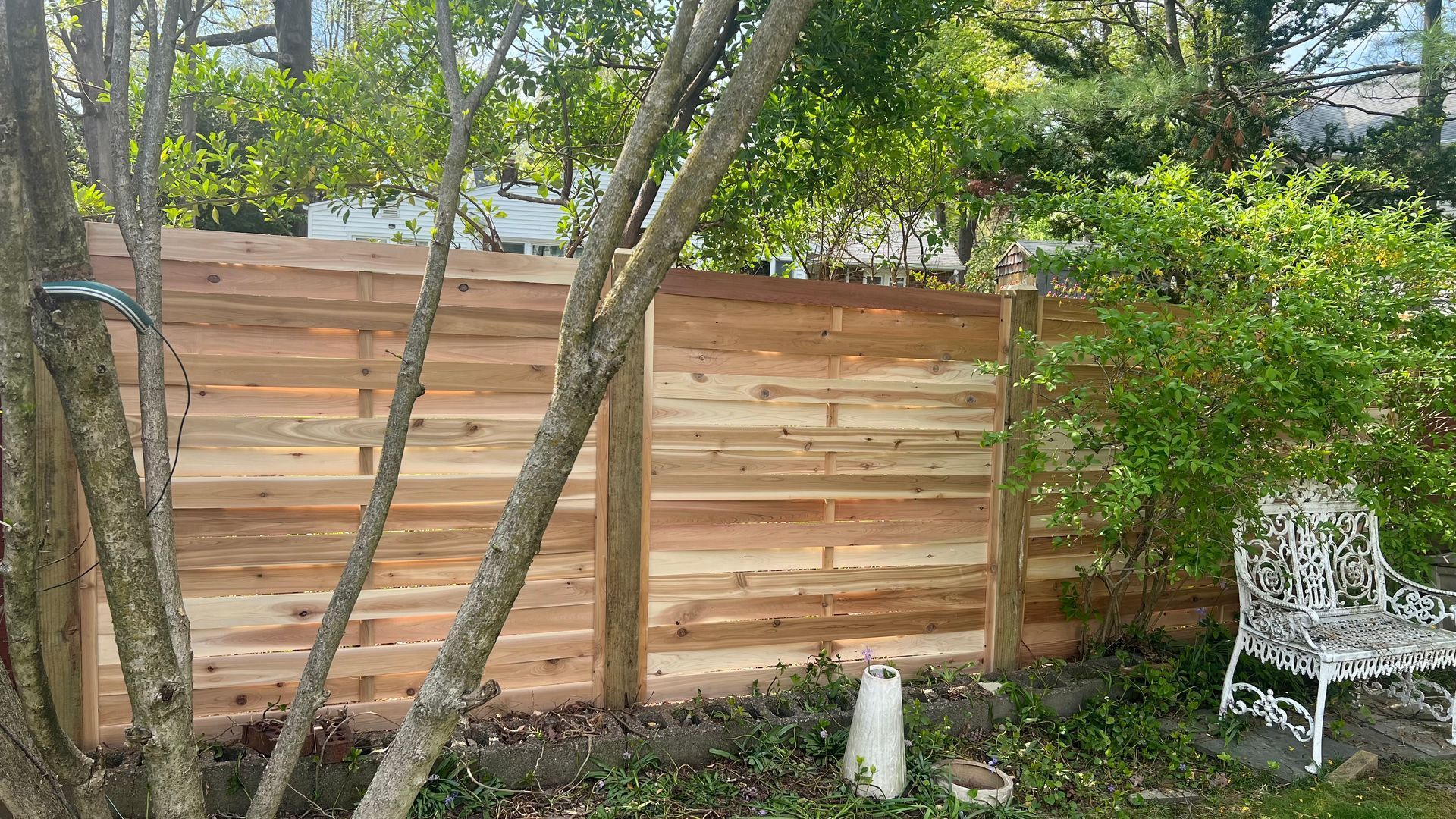 Wooden fence in a backyard setting with a white bench and trees.