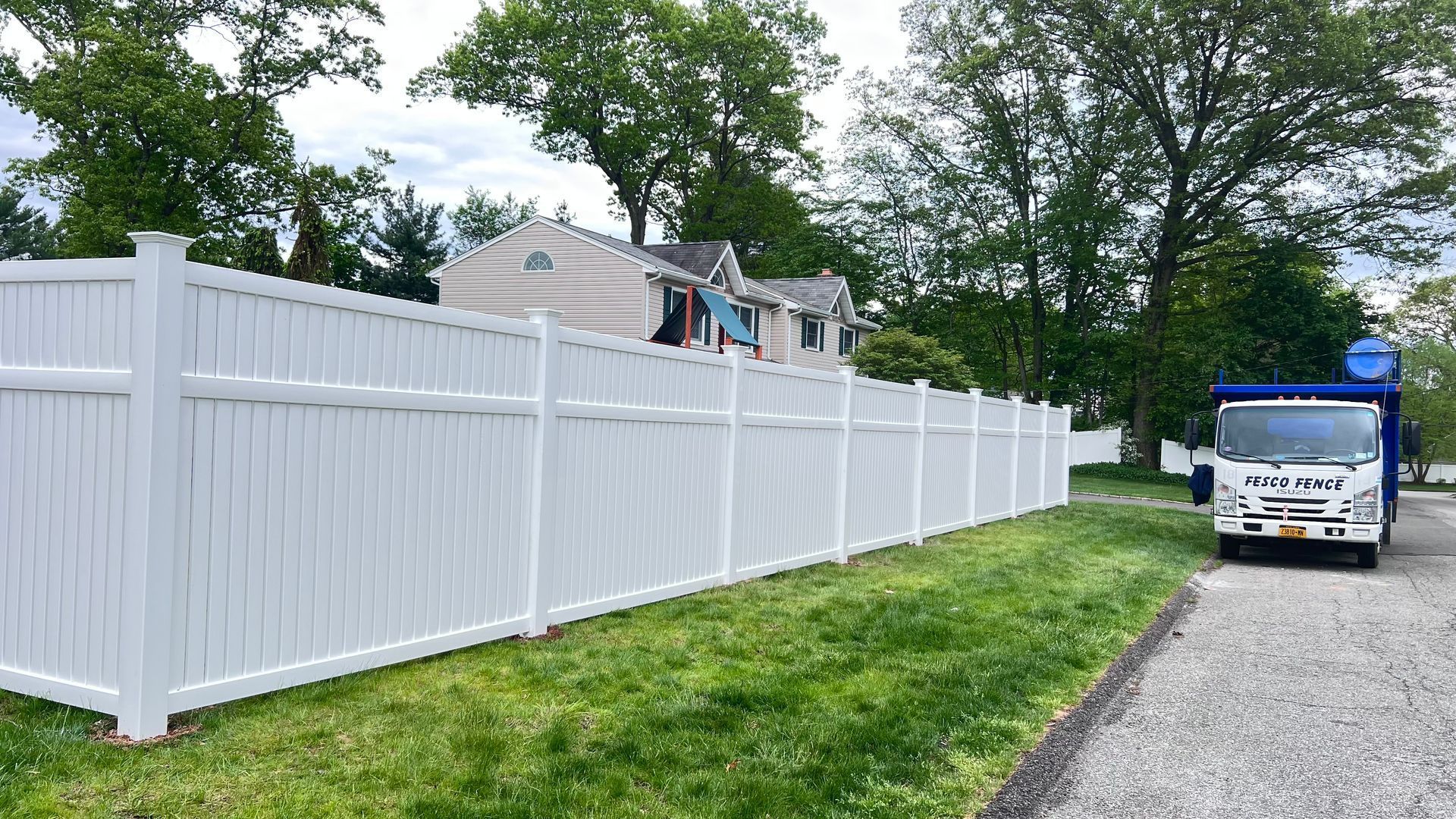 White vinyl fence along grassy lawn, with a truck parked on gravel driveway.