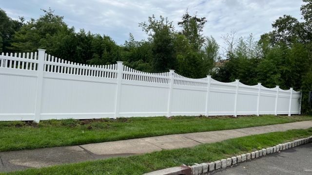 White vinyl fence with decorative top, along a grassy verge and sidewalk.