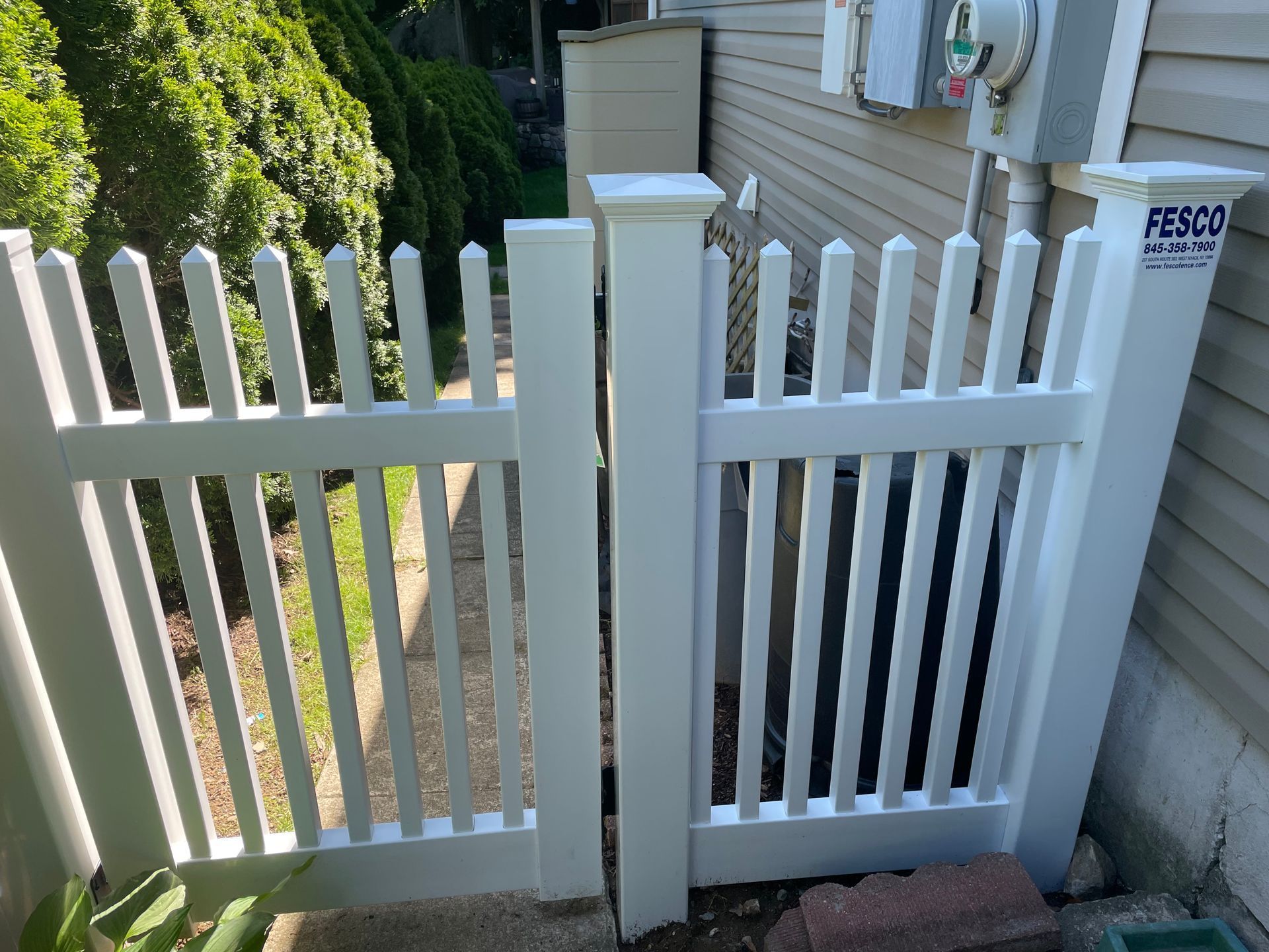 White picket fence with gate opening onto a walkway, next to a building.