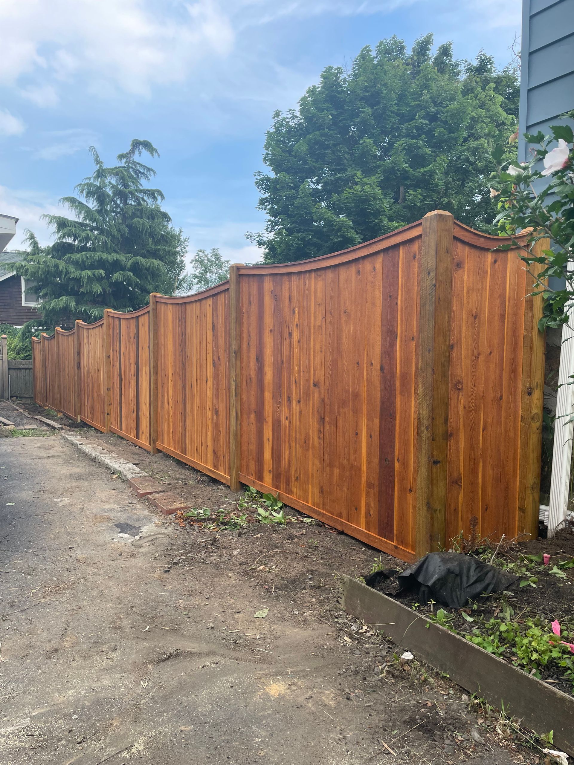Wooden fence stained brown, with curved top design, outdoors on a cloudy day.