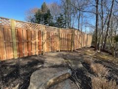 Wooden fence in a yard with rocks and trees.