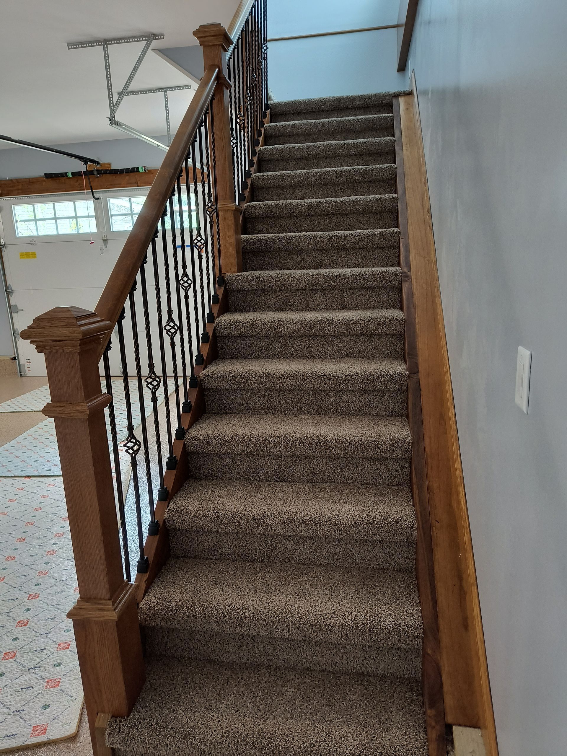 Wooden staircase with brown carpet, iron railing, leading upwards.