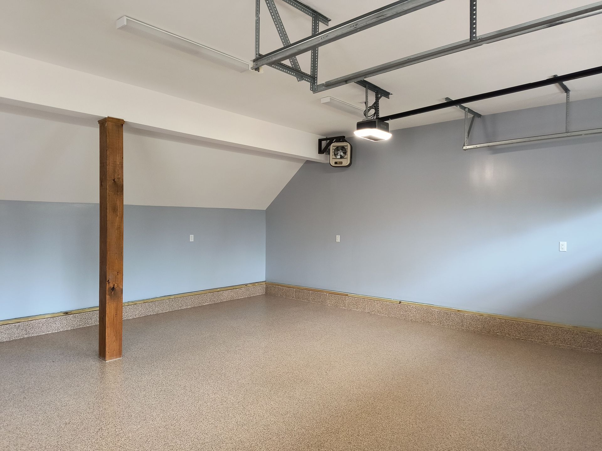 Empty garage with blue-gray walls, speckled floor, wooden support beam, and overhead door track.