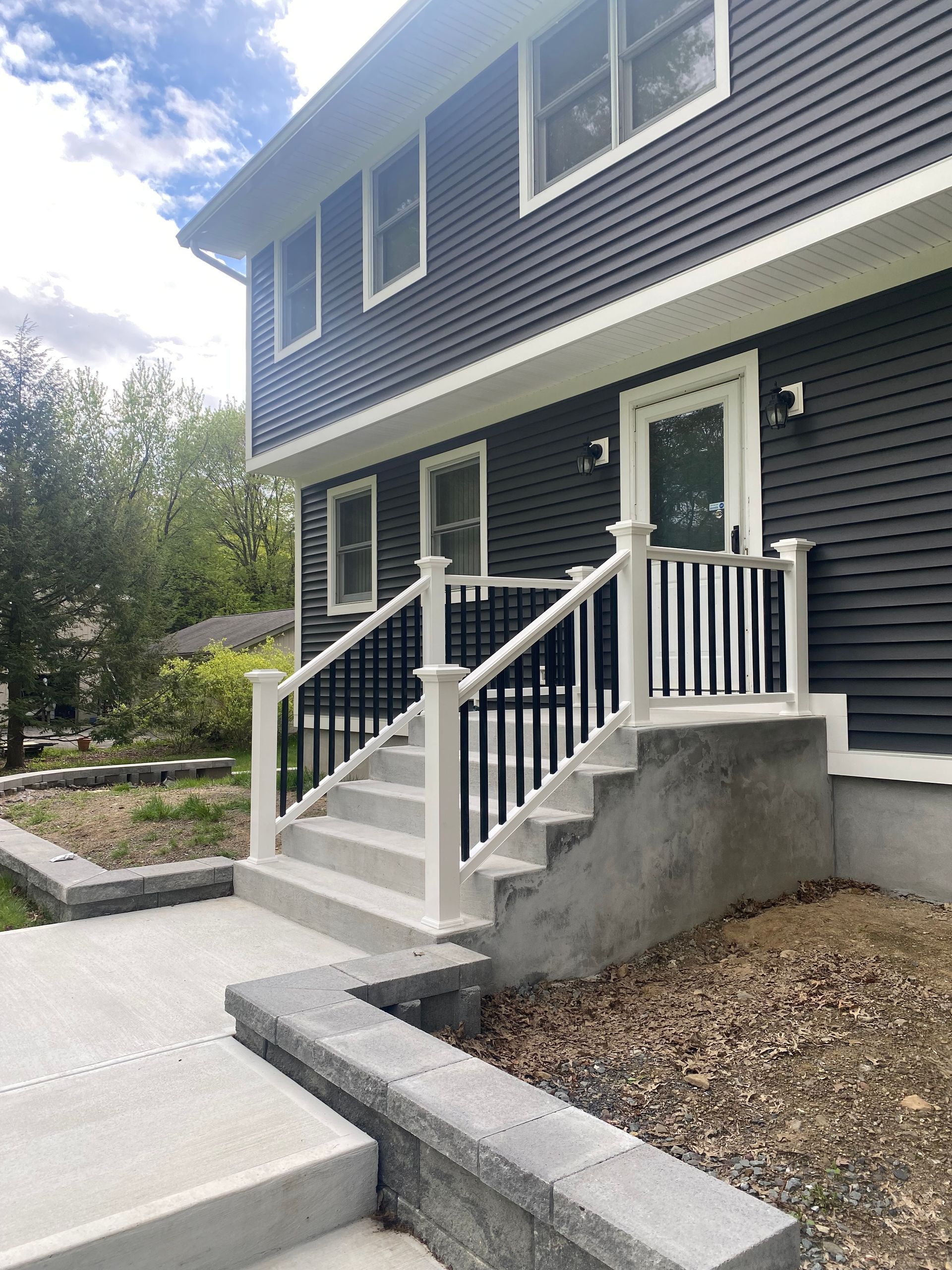 Gray house with steps leading up to the front door, black railings, and a concrete pathway.