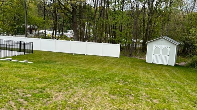 Green yard with white fence and shed; trees in the background.