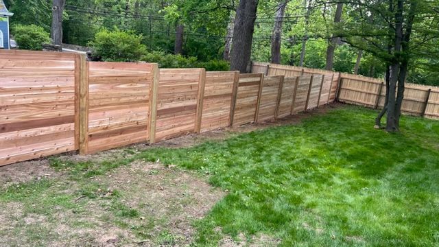 A wooden privacy fence in a backyard, surrounded by green grass and trees.