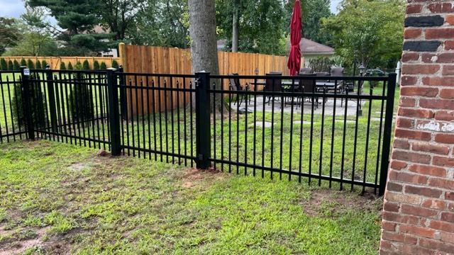Black metal fence in a yard, with a wooden fence and red umbrella visible in the background.